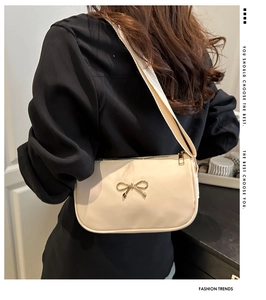 Close-up of cream shoulder bag with golden bow buckle detail and fabric strap