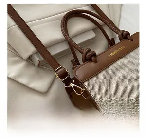 Close-up of golden hardware hooks and leather handles on a beige canvas handbag