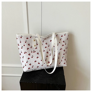 Detailed view of the white cherry print tote bag on a textured wooden pedestal
