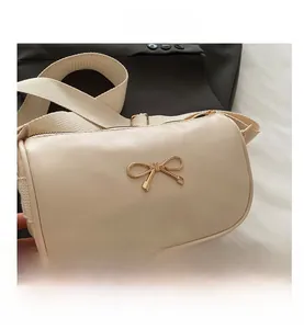 Detail showing beige PU leather bag with golden bow and white canvas shoulder strap