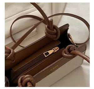 Close-up of contrast tote bag featuring a gold zipper closure and knotted strap detail