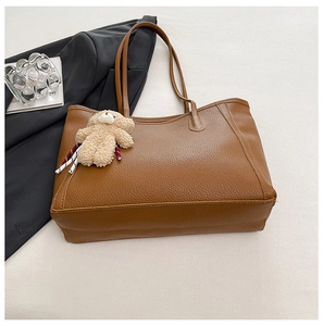 Grand sac cabas marron foncé avec pendentif ours en peluche sur un bureau blanc