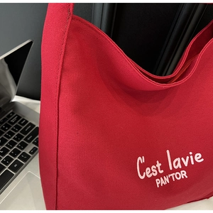 Close-up of red canvas tote bag featuring white embroidered C'est lavie PAN'TOR lettering