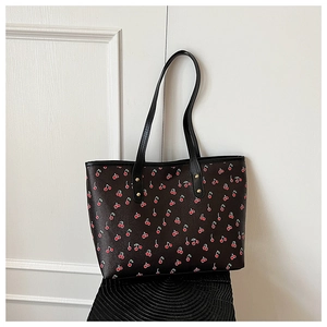 Close-up of red cherry pattern on black tote bag with gold rivets on straps