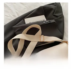 Detail showing the wide fabric shoulder strap and golden bow hardware on the handbag