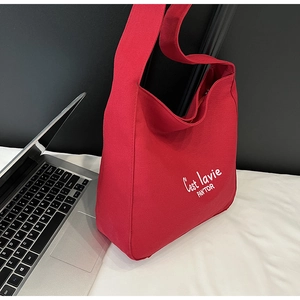 Detail of red canvas tote bag featuring white C'est lavie script and wide shoulder strap