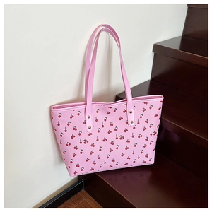 Close-up of pink tote bag with red cherry prints and golden rivets on leather straps