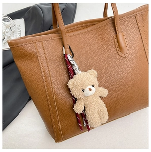 Close-up of brown litchi grain leather tote bag with a plush bear charm detail