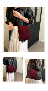 Detail of burgundy fringe bucket bag with suede texture and long tassels on shoulder strap