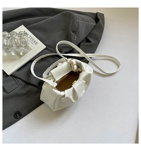 Detail of white pleated cloud bag featuring pearl handle and detachable crossbody strap