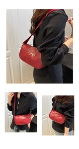 Detailed view of red faux leather shoulder bag with decorative gold bow buckle
