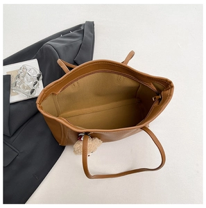Deep brown pebbled leather tote bag with zip closure and plush bear charm on white background