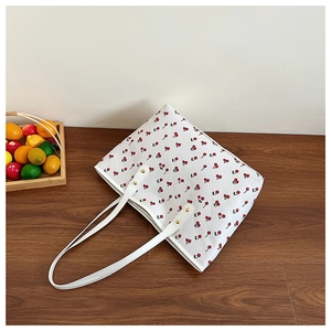 Top view of white canvas tote bag with red cherry prints and leather straps on wood floor