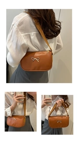 Detail of brown rectangular bag with golden metal bow and wide fabric shoulder strap