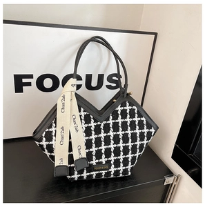 Détail du cabas en tweed noir et blanc avec poignées en cuir et ruban décoratif élégant