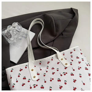 Detailed macro of white tote bag with red cherry prints and golden metal rivet hardware