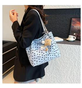 Détail d'un sac cabas matelassé bleu clair avec motifs nœuds noirs et breloque ours en peluche
