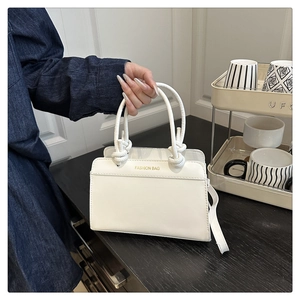 Detail of white leather tote bag featuring a creative woven rope handle and gold lettering