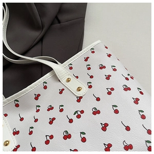 Close-up of cherry print on white leather tote bag with gold metal rivet details