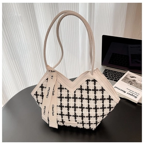 Détail du sac cabas en tweed à carreaux avec anses en cuir et ruban décoratif sur le bureau
