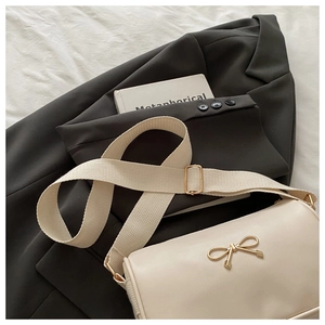 Detail of cream crossbody bag with golden bow buckle and wide canvas shoulder strap