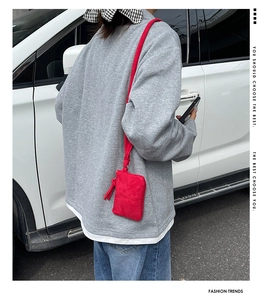 Outdoor close-up of a red suede crossbody mini bag with tassel zipper and shoulder strap