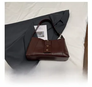 Close-up of brown glossy shoulder bag with gold metal eyelet straps and size comparison