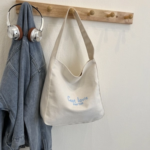 Chic cream canvas tote bag with light blue lettering hanging on a wooden stand
