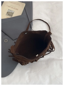Detail view of brown suede bucket bag featuring long fringe and silver magnetic closure