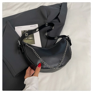 Detail of black faux leather half-moon bag with silver metal chain and wide grommet strap