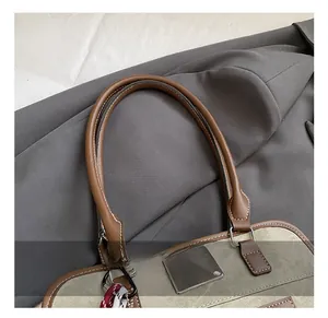 Gros plan des poignées en cuir marron avec surpiqûres blanches et ferrures sur le sac
