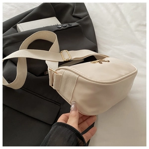 Close-up of beige crossbody bag with wide fabric strap on a minimalist blazer backdrop