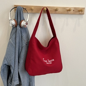 Red canvas tote bag with white lettering hanging on a hook in a minimalist interior