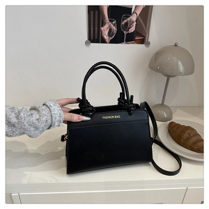Detail of black faux leather tote bag with knot handles and gold lettering on a desk
