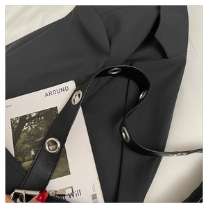 Detail of black leather shoulder bag with silver metal eyelets on the strap over a blazer