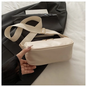 Detail of cream crossbody bag with wide woven strap and golden buckle on black suit