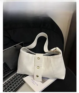 Chic white leather underarm bag with gold eyelet details shown in a modern office setup