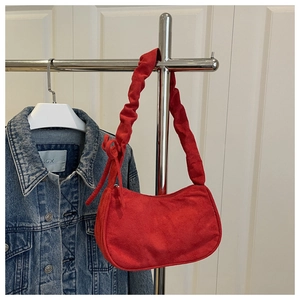 Détail du sac demi-lune en daim rouge avec bandoulière plissée et nœud sur le côté