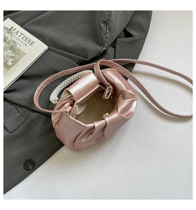 Detail of pink pleated cloud bag with pearl handle and gold magnetic closure on blazer