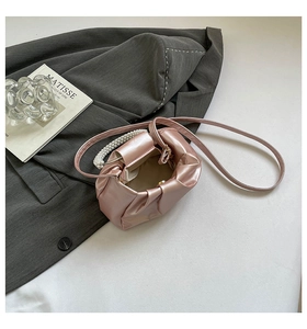 Detail of pink pleated cloud bag with pearl handle on grey blazer backdrop