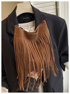 Gros plan du sac seau en daim marron avec longues franges sur un costume élégant