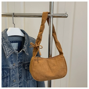Détail d'un sac sous le bras en daim marron avec un nœud sur la bandoulière et zip