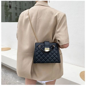 Close-up of quilted pattern and gold metal lock on black chain shoulder bag for women