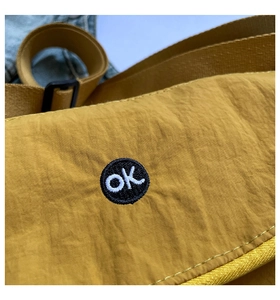 Detail of mustard yellow nylon crossbody bag with 'ok' circle embroidery and water-resistant texture