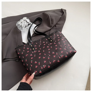 Detailed macro view of red cherry print on black textured leather tote bag with gold rivets