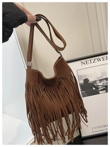 Detail of brown suede crossbody bag featuring long bohemian tassels and narrow shoulder strap