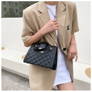 Detail of black quilted chain bag with gold hardware worn on a khaki blazer