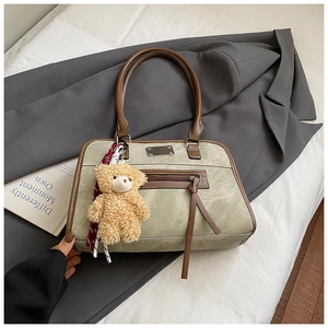Détail du sac à main vert sauge avec charm ours en peluche et poignée en cuir marron