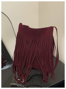 Détail du sac seau en daim bordeaux avec de longues franges sur une table noire