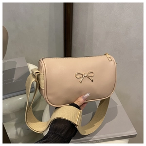 Detail of beige cylinder bag with golden bow ornament and wide adjustable strap